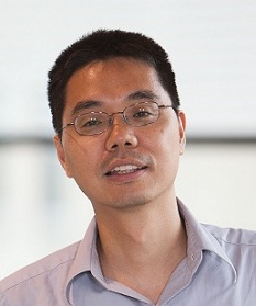 Menggang Yu slightly smiles as he wears wire glasses and a light colored button-up shirt.