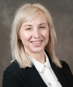 Amanda DeWitt smiles as she wears a white button up and a black blazer. She has light blond hair.