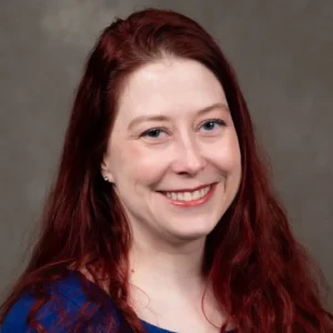 Colleen Baldwin is smiling and has long red hair. Colleen wears a blue shirt.