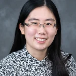 Sarah Lim smiles for her bio picture. She has long, black hair parted in the middle She is wearing glasses and a black and white patterned blouse.