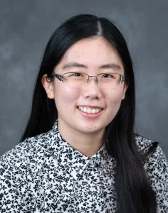 Sarah Lim smiles for her bio picture. She has long, black hair parted in the middle She is wearing glasses and a black and white patterned blouse.