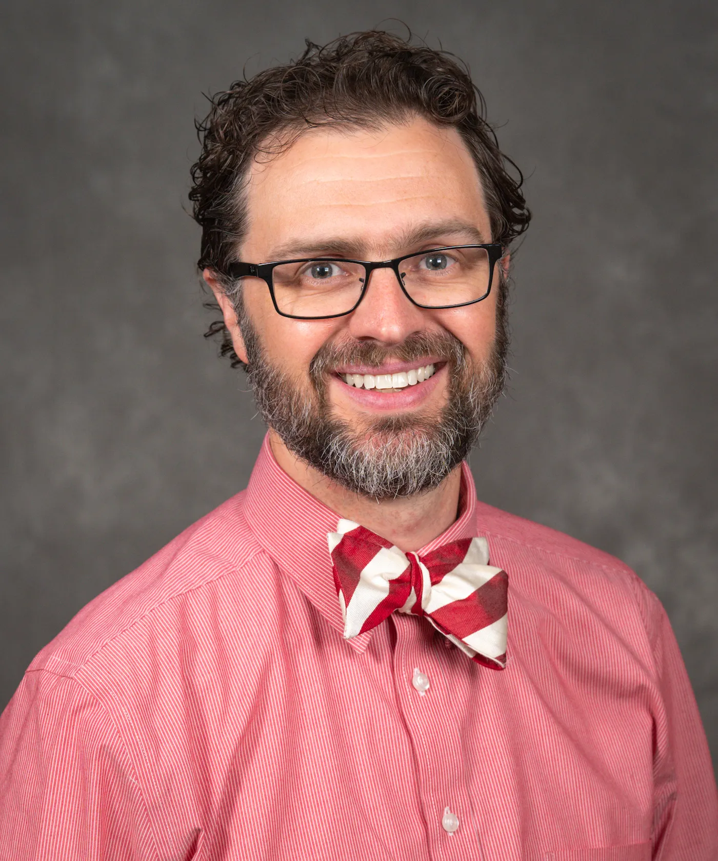 William Buckingham's bio headshot. Will wears a light red/pink shirt and smiles. Will also has a red and white bowtie.