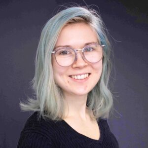 Julia smiles. She has large glasses and light blue hair.