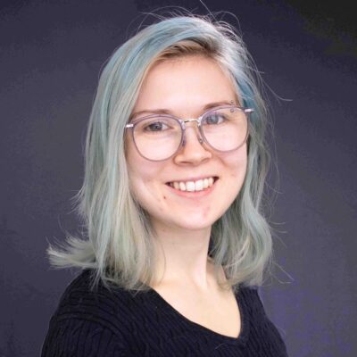 Julia smiles. She has large glasses and light blue hair.