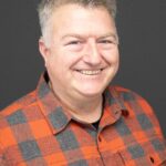 Dave smiles and wears bright plaid. Dave has short, greying hair.