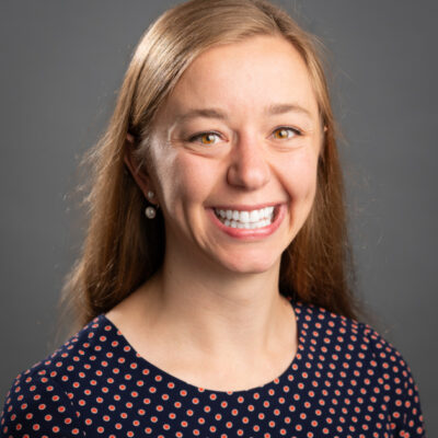 Eleanna smiles brightly for her bio picture. She wears polka dots and has long, light brown hair.
