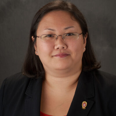 Jenny smiles slightly for her headshot. She has glasses, long dark hair, and wears a professional black blazer.