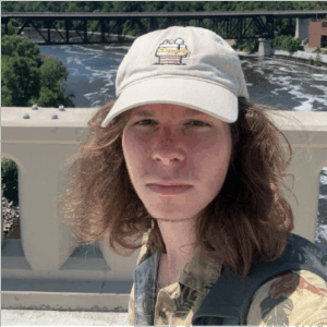 Young man with long hair and a baseball cap faces the camera.