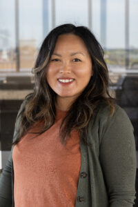 A woman with golden brown long hair smiles while facing the camera. 