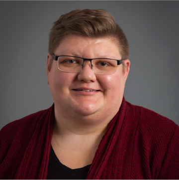 A person with short, cropped hair and glasses and wearing a burgundy shirt smiles for a professional headshot.